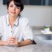 Hispanic woman smiling while leaning on a kitchen counter, enjoying a bright day indoors.
